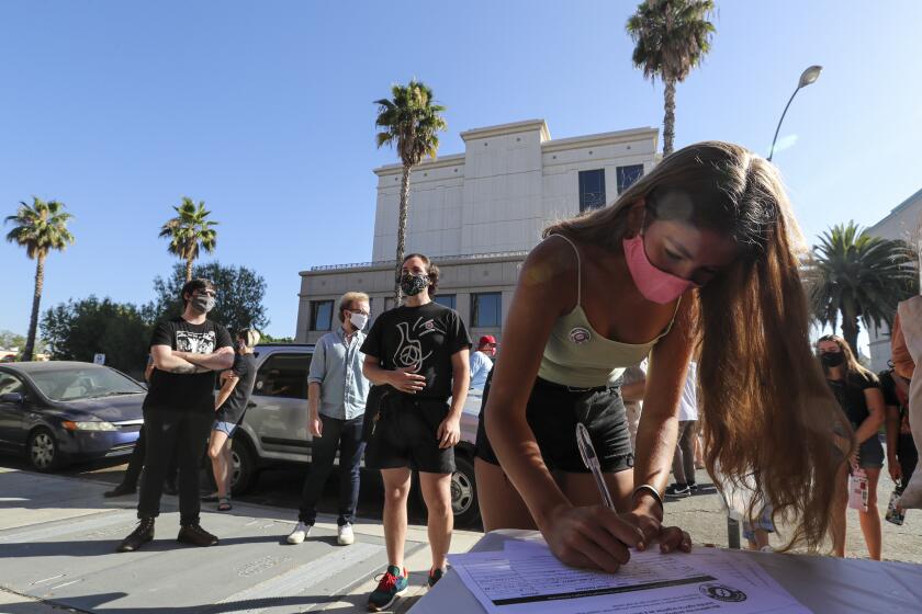 RIVERSIDE, CA - JULY 10: Hope Macias signs a petition drive organized by Augie's workers in front of the Riverside location asking people to sign a petition demanding that Augie's Coffee House to reopen. Riverside County chain recently shut down for what they say is coronavirus but whose former workers claim was in retaliation forming Augie's Union. Augie's Coffee House on Friday, July 10, 2020 in Riverside, CA. (Irfan Khan / Los Angeles Times)