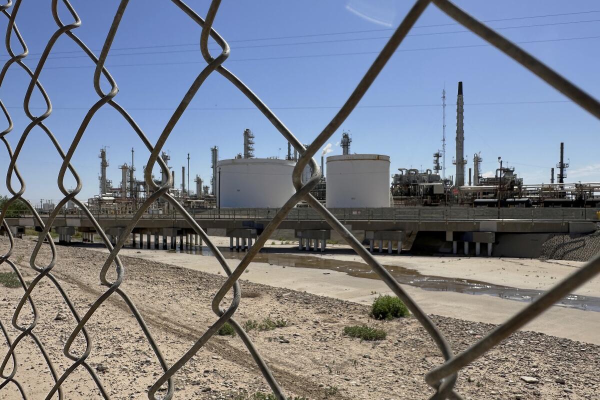 A chain link fence borders a large refinery