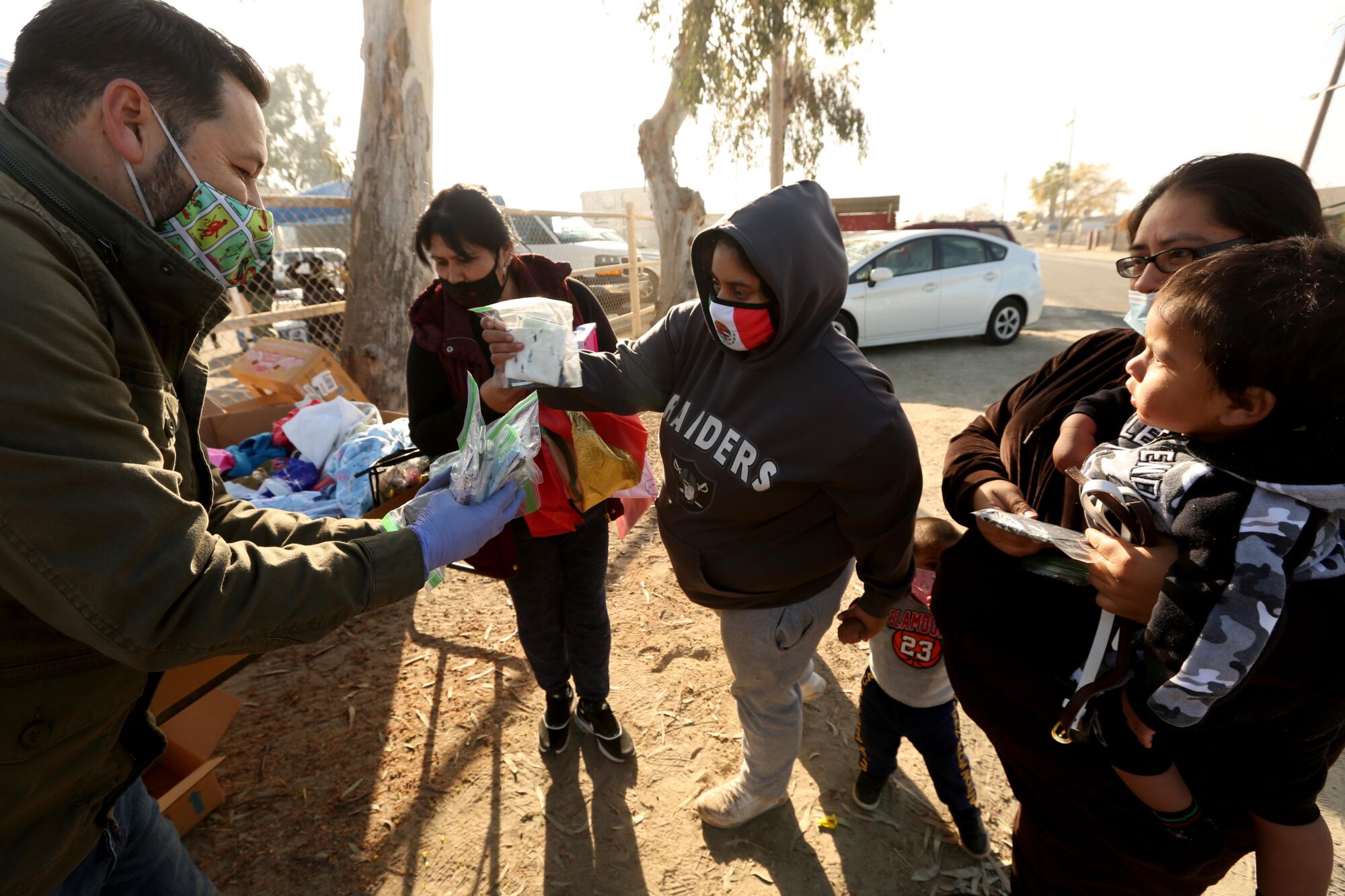 A man hands out masks to families standing in a dusty field