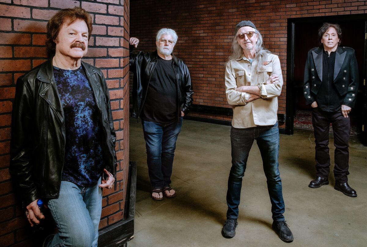 Four men from a rock band stand in front of brick walls in a hallway
