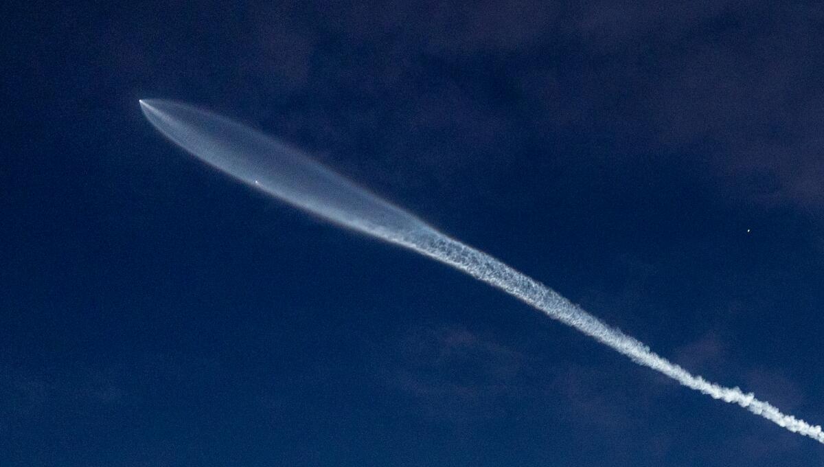 A rocket and contrail are seen in a dark sky.