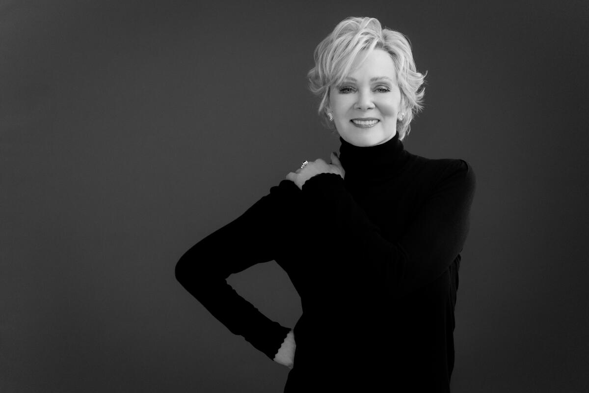 Jean Smart poses for a portrait wearing a turtleneck, one hand on hip and the other on her shoulder.