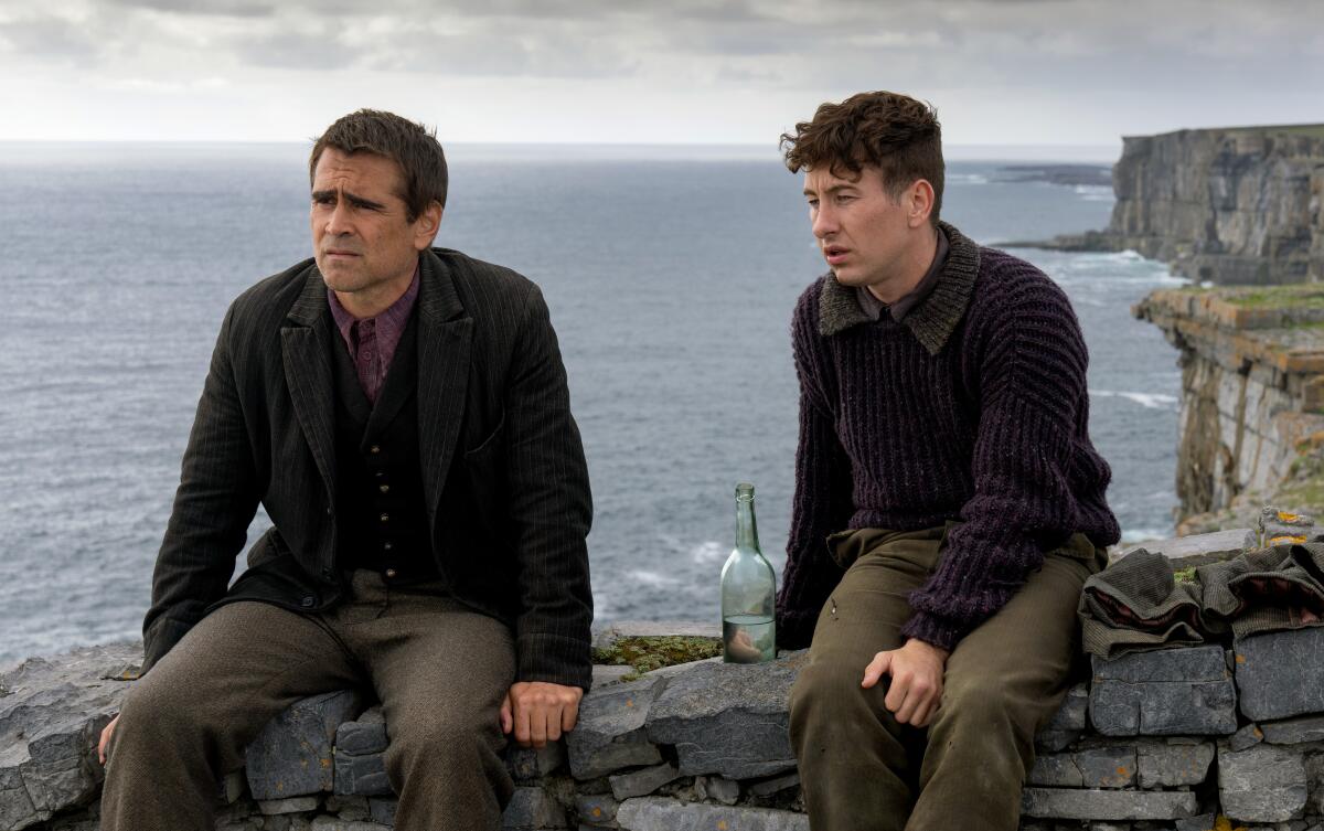 Two men sit on a stone wall above the sea in a scene from "The Banshees of Inisherin."