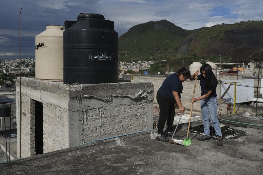 Sonia Estefanía Palacios Díaz, izquierda, y Lizbeth E. Pineda Castro, derecha, barren el techo de una casa utilizada para captar agua de lluvia en el distrito de Iztapalapa, el domingo 21 de julio de 2024, en Ciudad de México. (AP Foto/ Marco Ugarte)