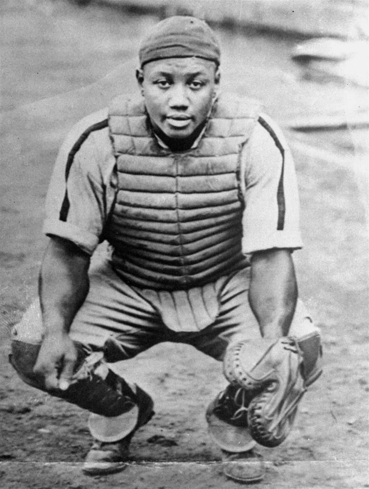 Negro Leagues legend Josh Gibson crouches on a field in catcher's gear.