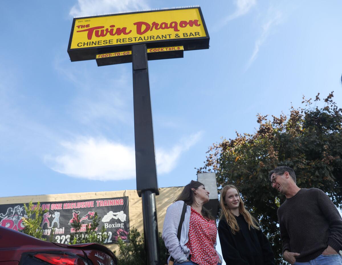 Three people stand under a tall sign with the words "Twin Dragon."