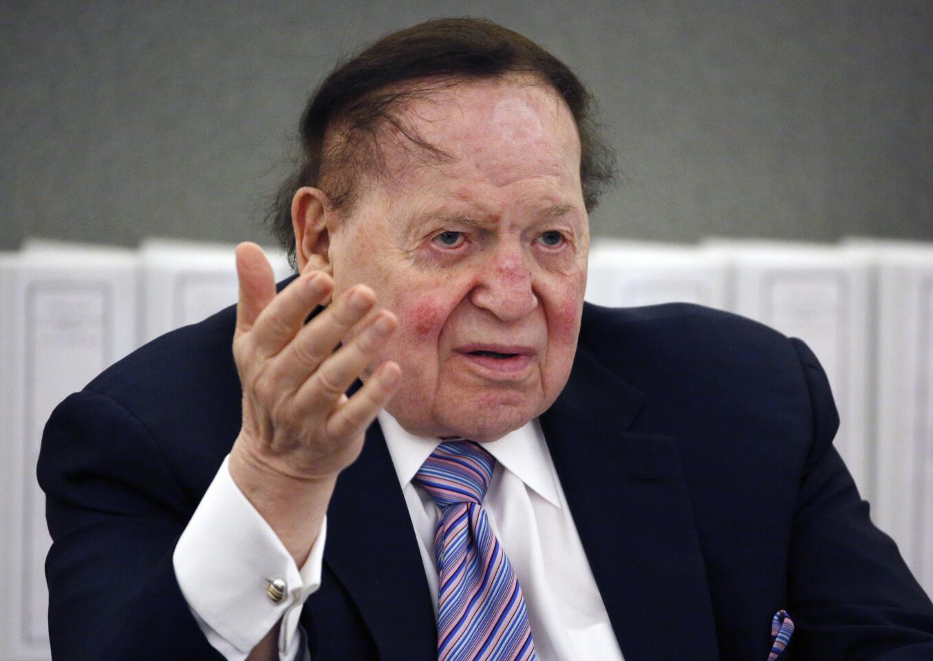 Sheldon Adelson, seated, gestures with one hand as he speaks.