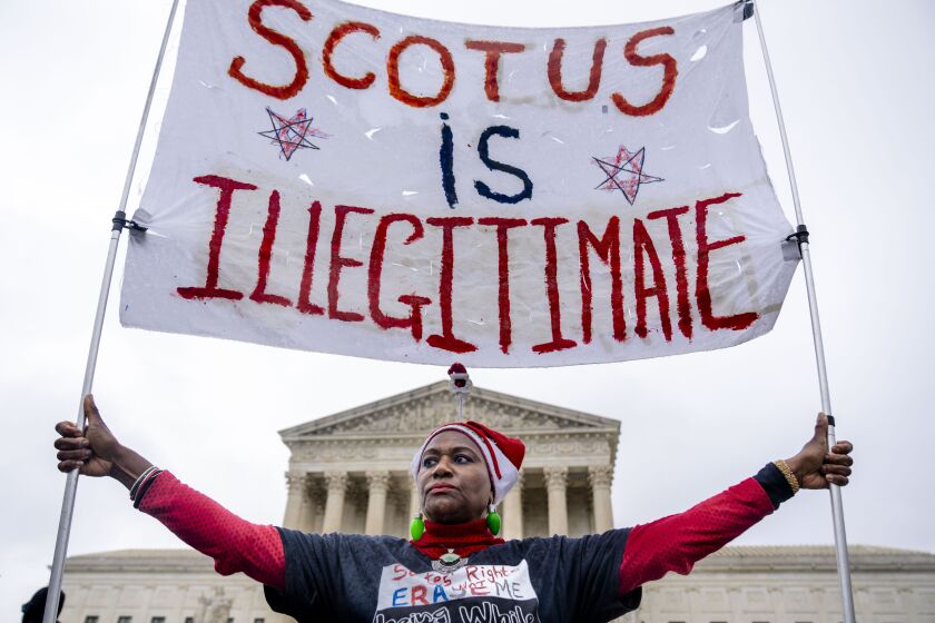 Nadine Seiler of Waldorf, Md., holds a sign that reads "SCOTUS is Illegitimate" in front of the Supreme Court in Washington, Wednesday, Dec. 7, 2022, as the Court hears arguments on a new elections case that could dramatically alter voting in 2024 and beyond. The case is from highly competitive North Carolina, where Republican efforts to draw congressional districts heavily in their favor were blocked by a Democratic majority on the state Supreme Court. (AP Photo/Andrew Harnik)
