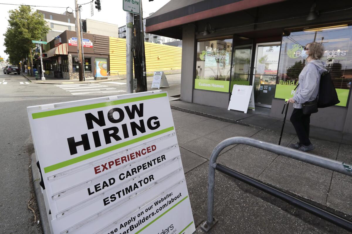 A pedestrian wearing a mask walks past a board advertising a job opening for a remodeling company June 4 in Seattle.