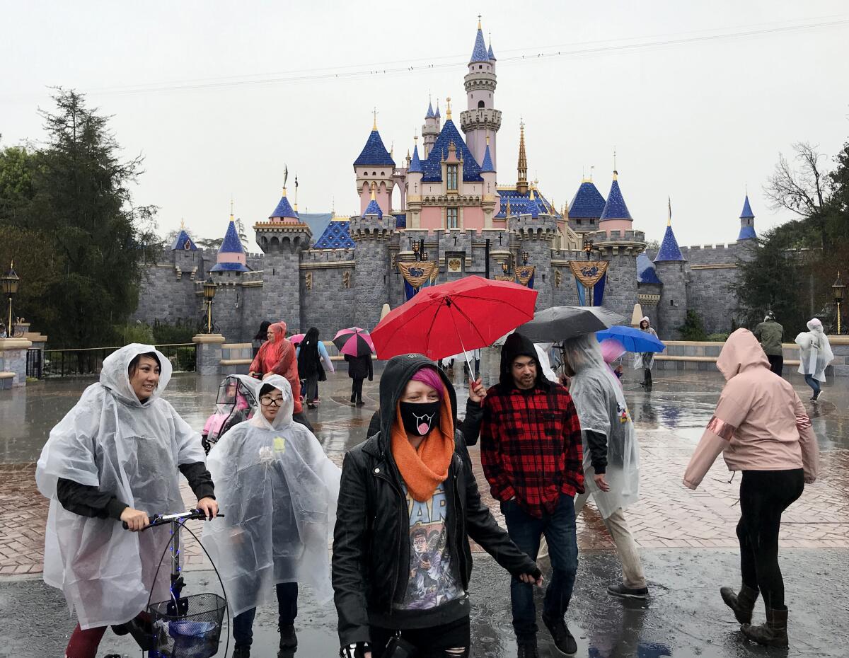 A guest wears a face mask in front of the Sleeping Beauty Castle while visiting Disneyland.