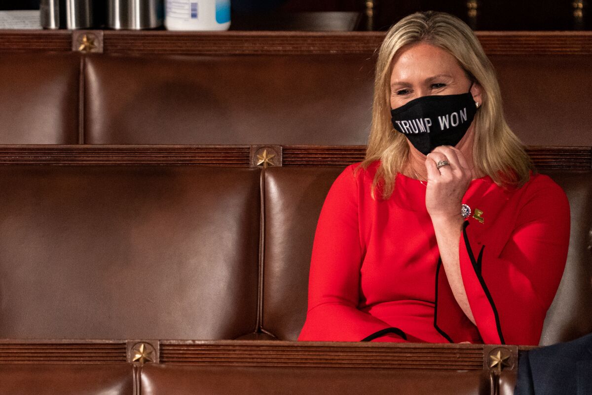 A woman in a red dress sits among rows of leather chairs wearing a face mask that reads "Trump won" 