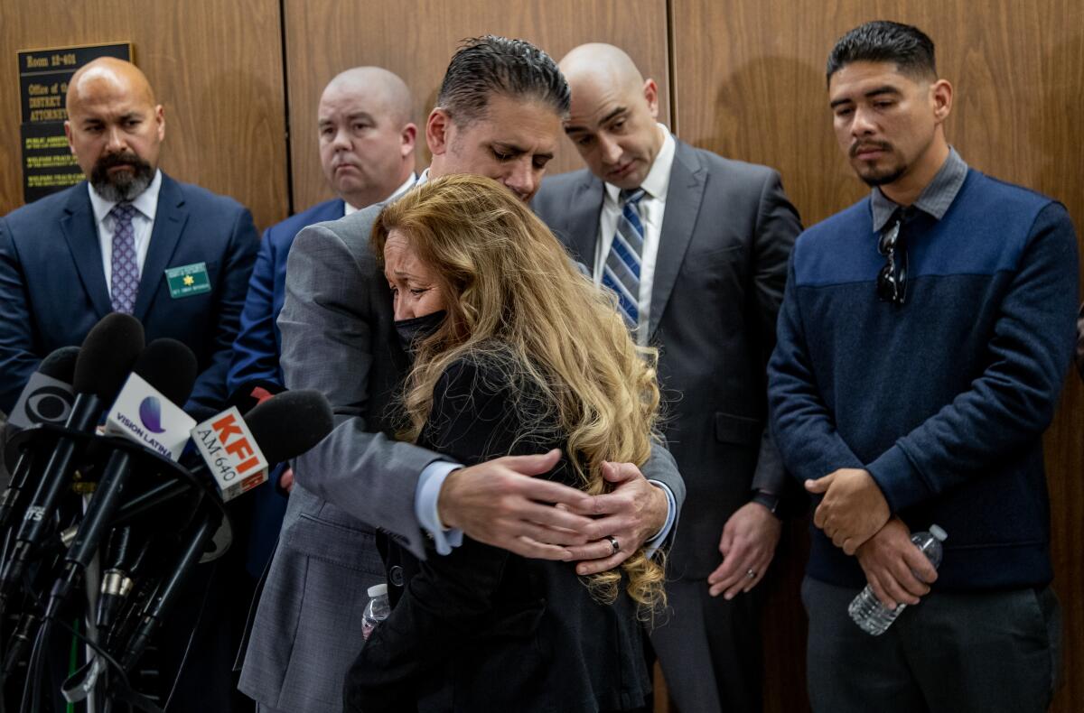 A man in a suit hugs a woman in a courtroom