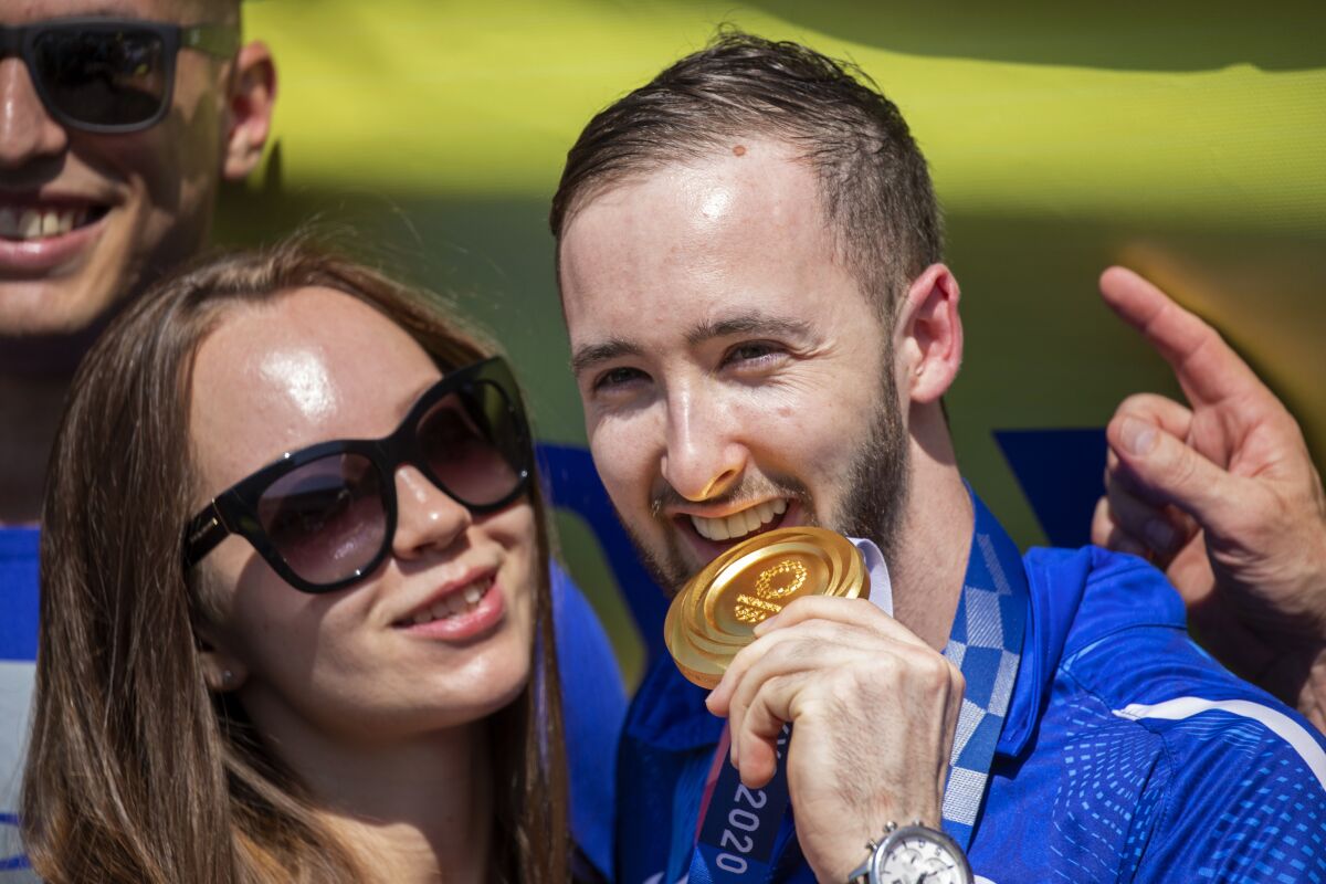 CORRECTS NAME TO ARTEM DOLGOPYAT - Artem Dolgopyat, Israeli artistic gymnastics men's gold medalist of Tokyo 2020, stands with his partner Maria Masha Sakovichas, while holding his medal on his arrival to Ben Gurion Airport, near Tel Aviv, Israel, Tuesday Aug. 3, 2021. The Ukrainian-born Israeli gymnast was hailed as a national hero for winning Israel's second-ever gold medal — and its first in artistic gymnastics. But the celebrations were tempered after his mother lamented that the country's authorities will not allow him to wed because he is not considered Jewish according to Orthodox law. (AP Photo/Ariel Schalit)