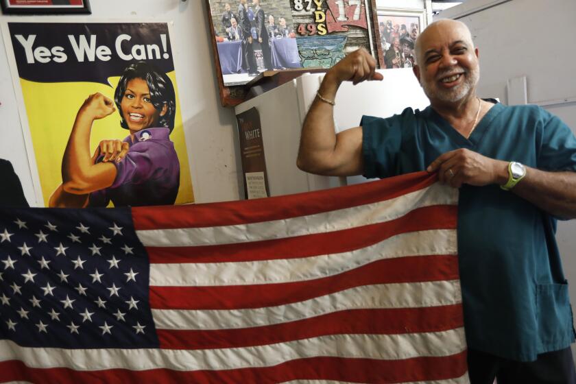 LOS ANGELES, CA - AUGUST 23, 2019 - - Lawrence Tolliver, 75, mimics a poster of Michelle Obama as Rosie the Rivetor that rests on one of the walls of his famed TolliverÕs Barber Shop in South Los Angeles on August 23, 2019. When Michelle Obama was brought up in conversation as a person who could beat Donald Trump denizens of the barbershop agreed. (Genaro Molina / Los Angeles Times)