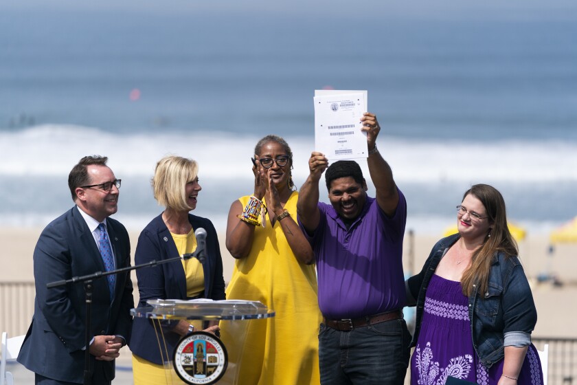 Anthony Bruce, second from right, a great-great grandson of Charles and Willa Bruce, holds up the title deed of the oceanfront property known as Bruce's Beach during a dedication ceremony in Manhattan Beach, Calif., Wednesday, July 20, 2022, as he is joined by wife, Sandra, from right, Los Angeles County officials, Holly J. Mitchell, Janice Hahn and Dean Logan. Los Angeles County officials on Wednesday presented the deed to prime California oceanfront property to heirs of the Black couple who built a beach resort for African Americans but were harassed and finally stripped of the land nearly a century ago. (AP Photo/Jae C. Hong)