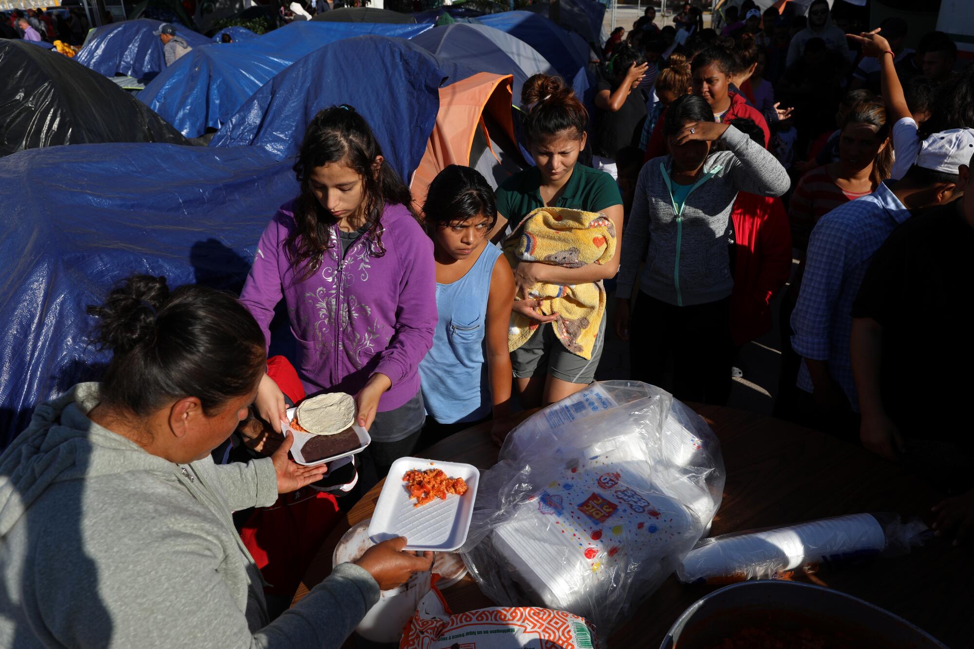 Los migrantes aguardan en fila mientras los voluntarios sirven el desayuno en un campamento casi a orillas de Río Grande en Matamoros, México.