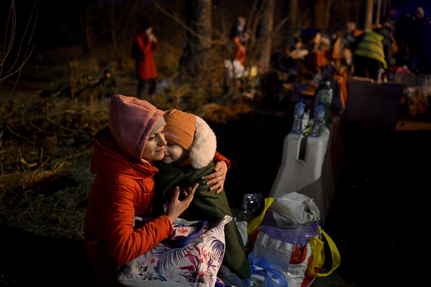 Una mujer carga a una niña después de cruzar la frontera de Ucrania hacia Rumania