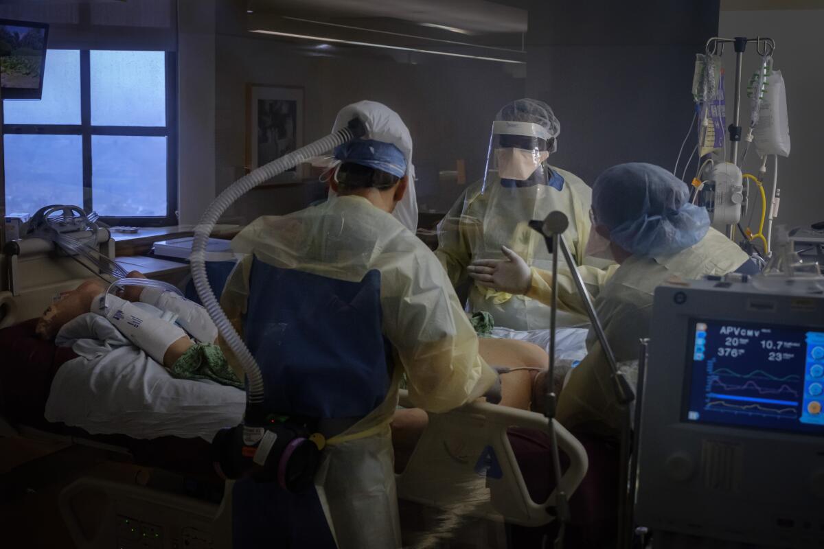 A patient, lying on his stomach on a hospital bed, is surrounded by medical personnel in protective gear.