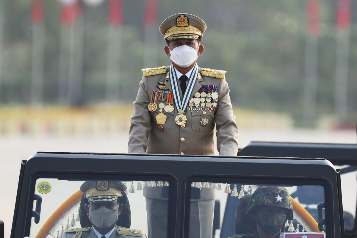 A masked general stands in a military truck.