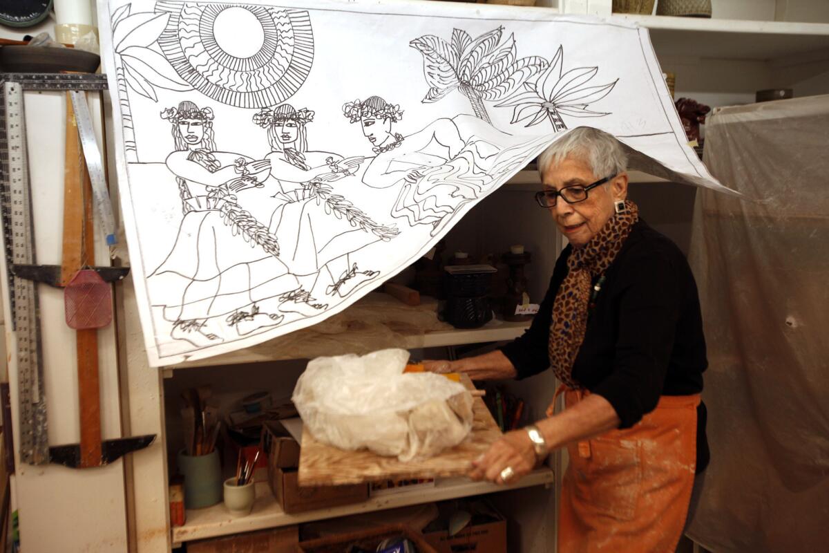 At Irving Place Studio in Los Angeles in 2014, Dora De Larios retrieves a piece of pottery from under a sketch from a large triptych she made for the Four Seasons Hotel in Hawaii called "Hawaiian Hula Dancers."