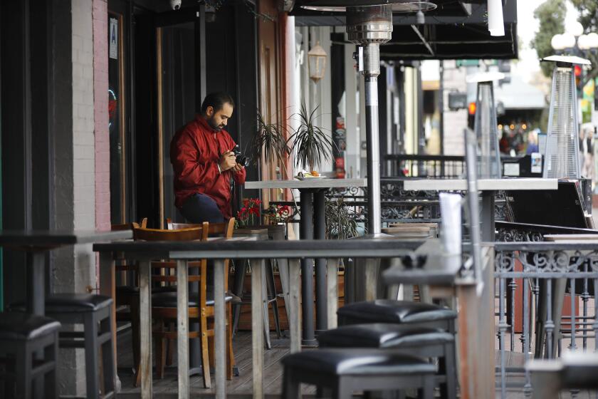 Surinder Singh, owner of Urban India restaurant in the Gaslamp Quarter, takes a photo of a dish to kill time with no customers in sight on March 16, 2020. Singh says he relies on conventioneers and downtown workers for business, but very few were to be found. Many restaurants in downtown were empty Monday afternoon.