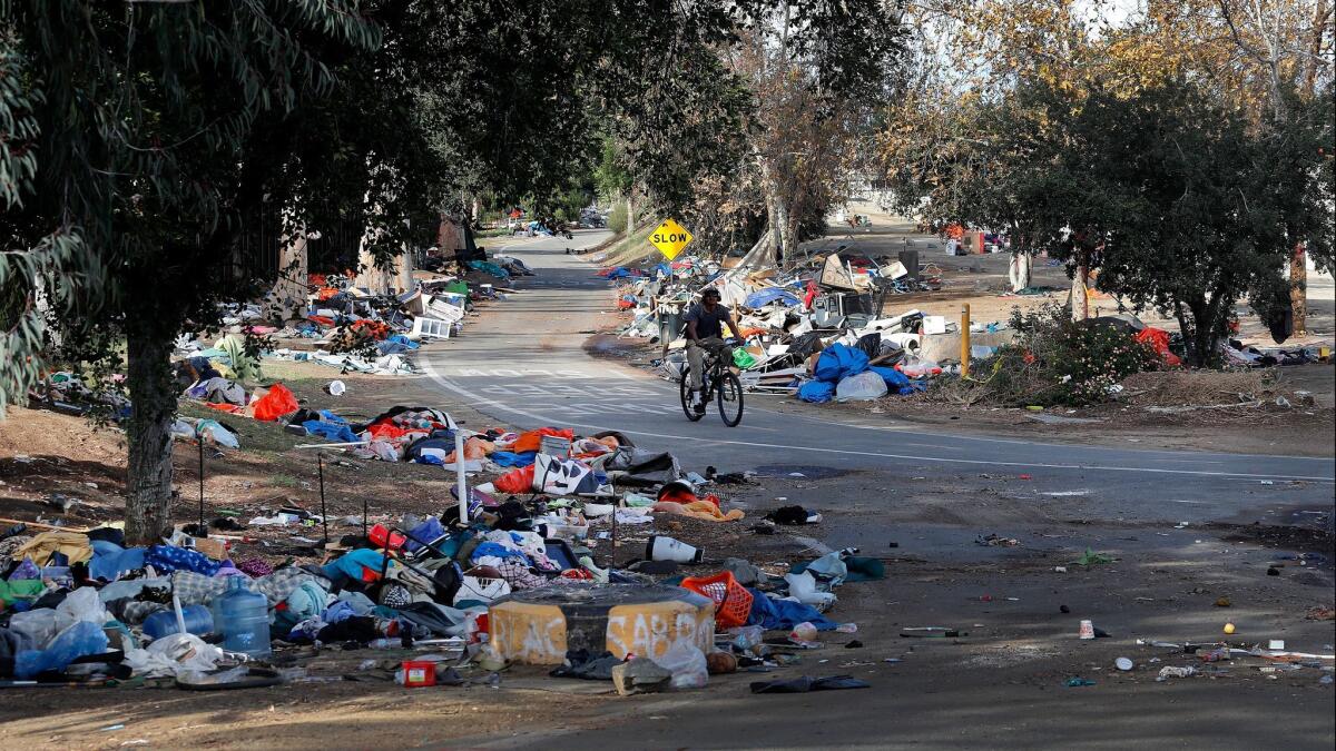A bicyclist rides past trash piles from the Santa Ana River homeless camp after it was cleared and more than 700 people relocated in Anaheim in February.