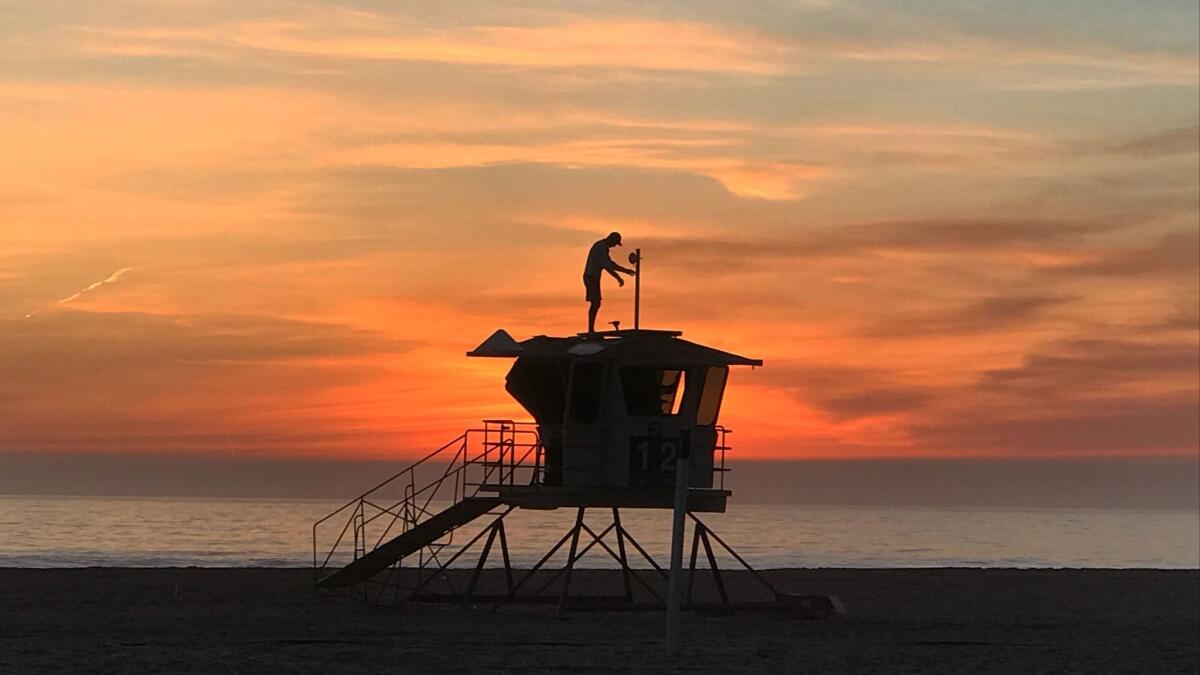 With the sunset behind him, Vitaliy Kostylov installs wireless communications technology and solar panels on a lifeguard tower at Huntington State Beach.
