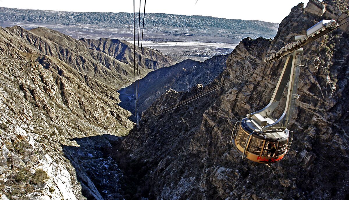 A tramway car hangs from cables extending from a desert valley up the side of a mountain