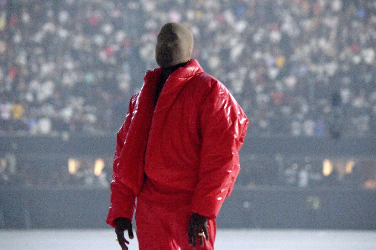 Kanye West wearing a red coat and pants and a mask over his face