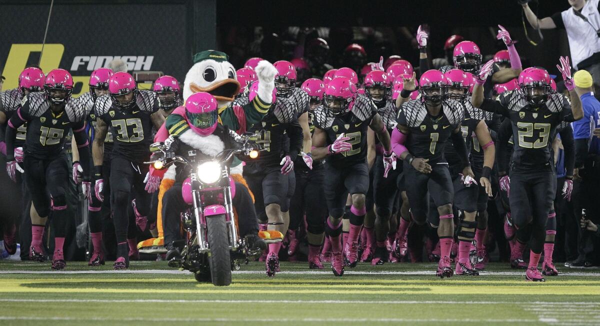 The Oregon football team rushes onto the field behind the Duck mascot riding a pink motorcycle in Eugene back in 2013.