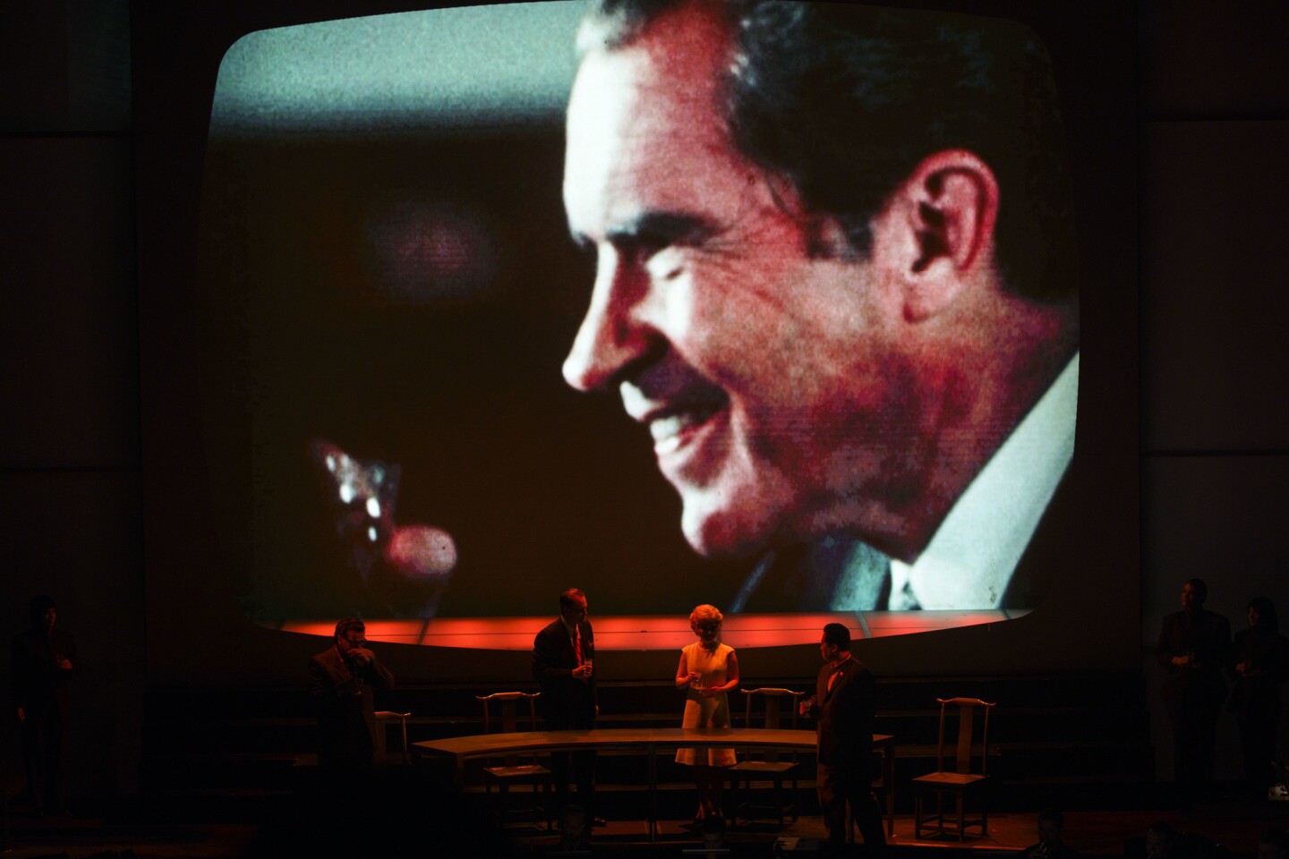 Ryan McKinny as Richard Nixon, left, Joélle Harvey as Pat Nixon, center right, John Matthew Myers as Mao, right, and Peter Coleman-Wright, left, perform with the L.A. Philharmonic as a large projection screen shows TV footage from China in a performance of "Nixon In China" at the Walt Disney Concert Hall on March 3, 2017, in Los Angeles.