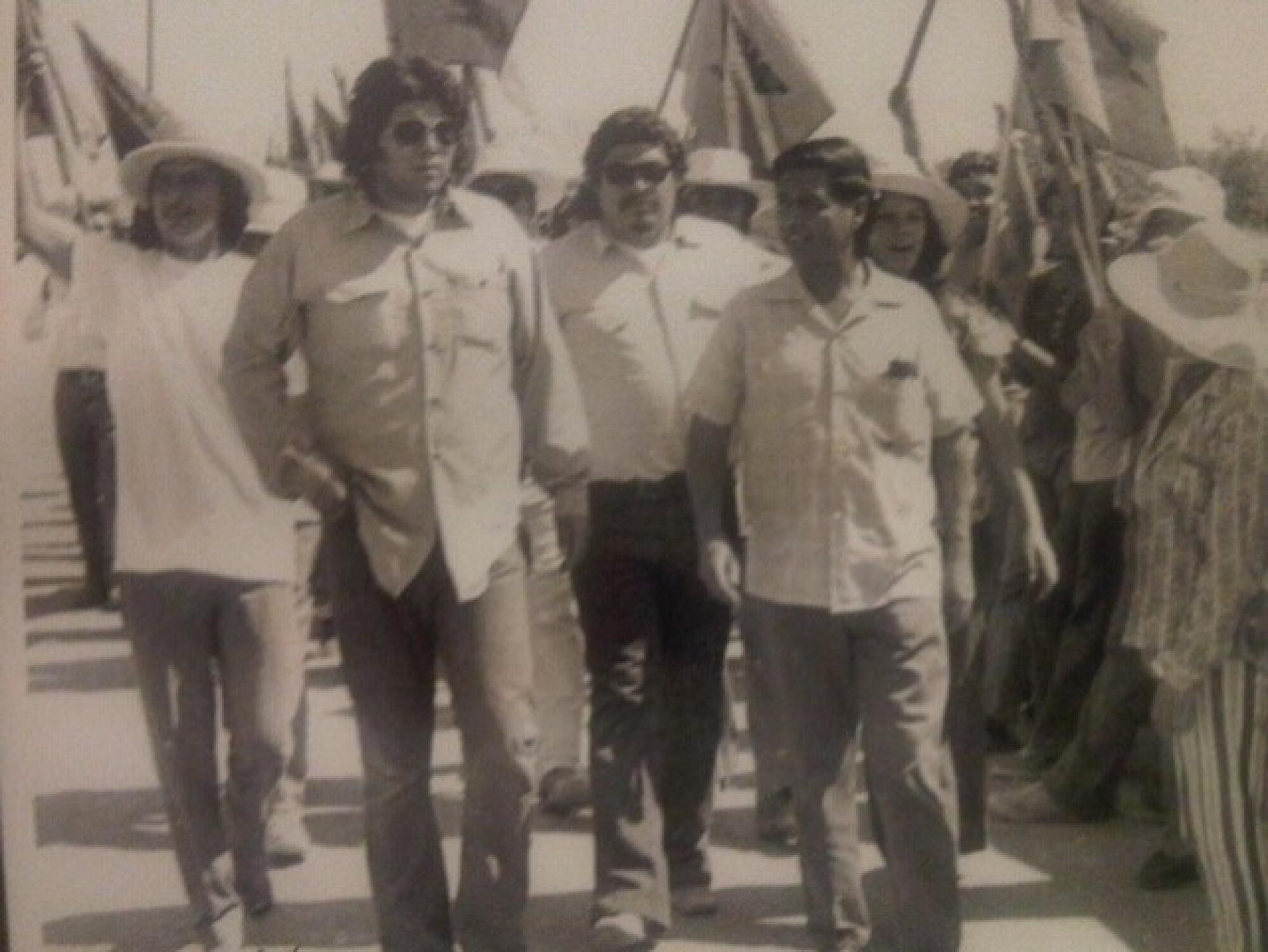 A sepia-colored photo of four people walking, with others behind them waving banners