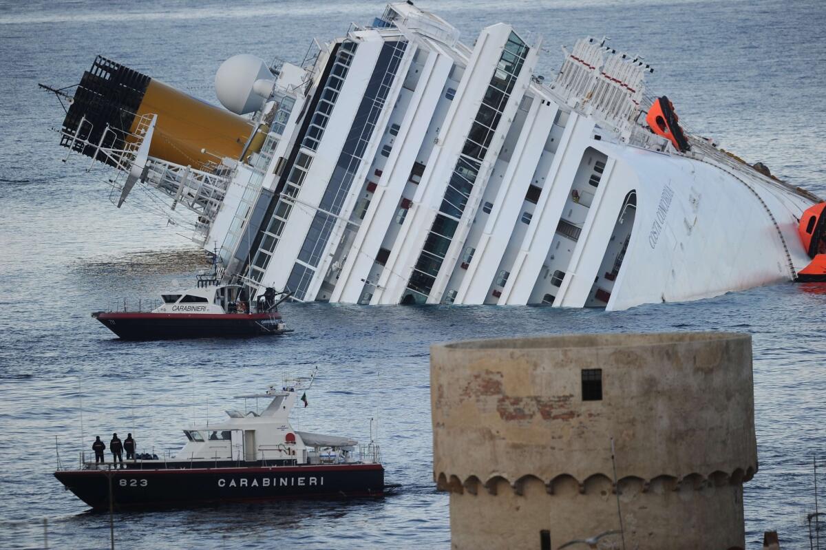 Boats of Italian police motor past the cruise liner Costa Concordia, aground in front of the harbor of Giglio island after hitting underwater rocks. An Italian court on Saturday convicted five crew members for their role in the disaster, which killed 32 people.