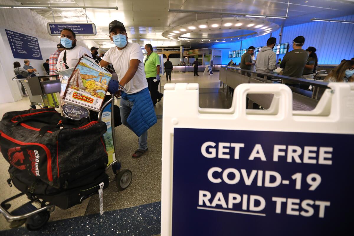 Airport travelers push carts past a sign offering a free COVID-19 rapid test