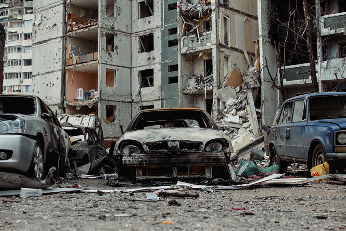 Badly damaged cars near a residential building after shelling