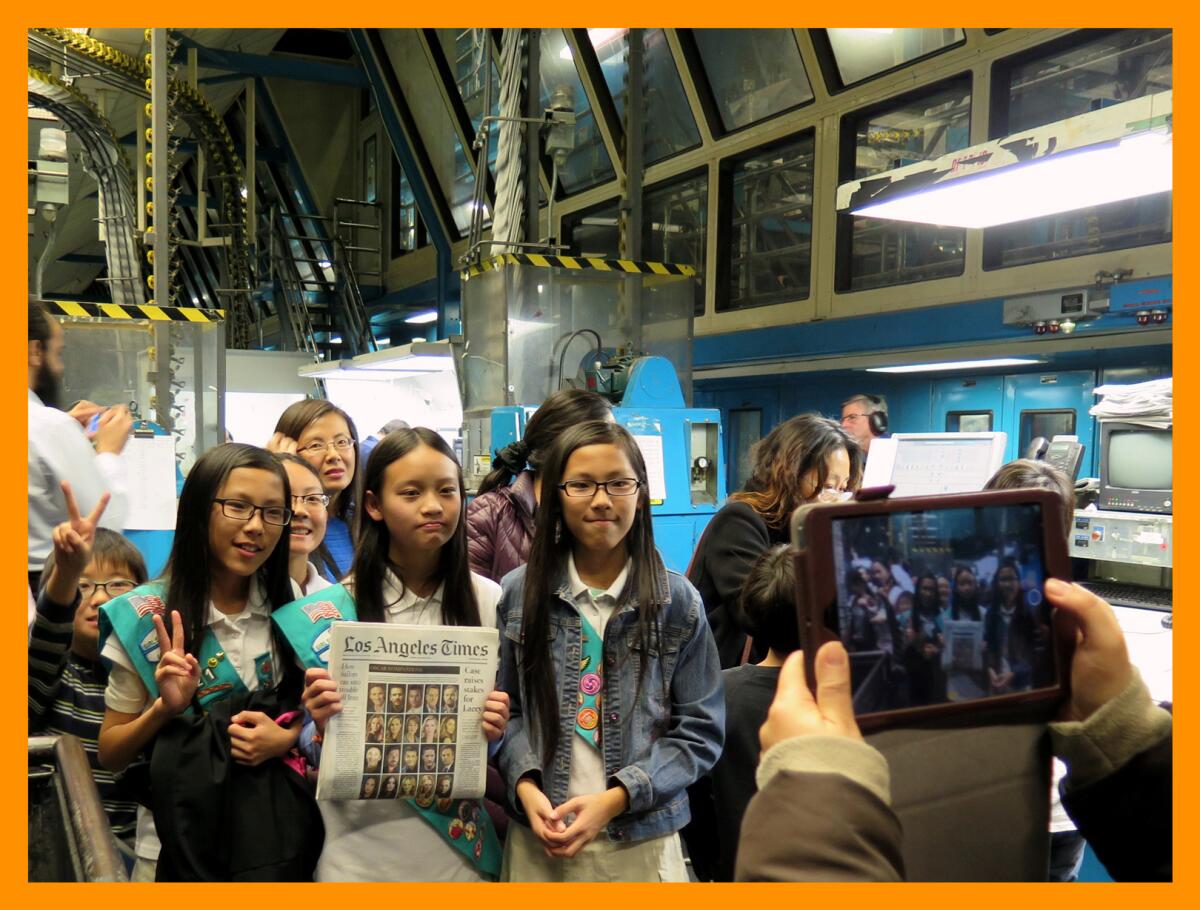 A group of Girl Scouts posing for a photo surrounded by printing press equipment
