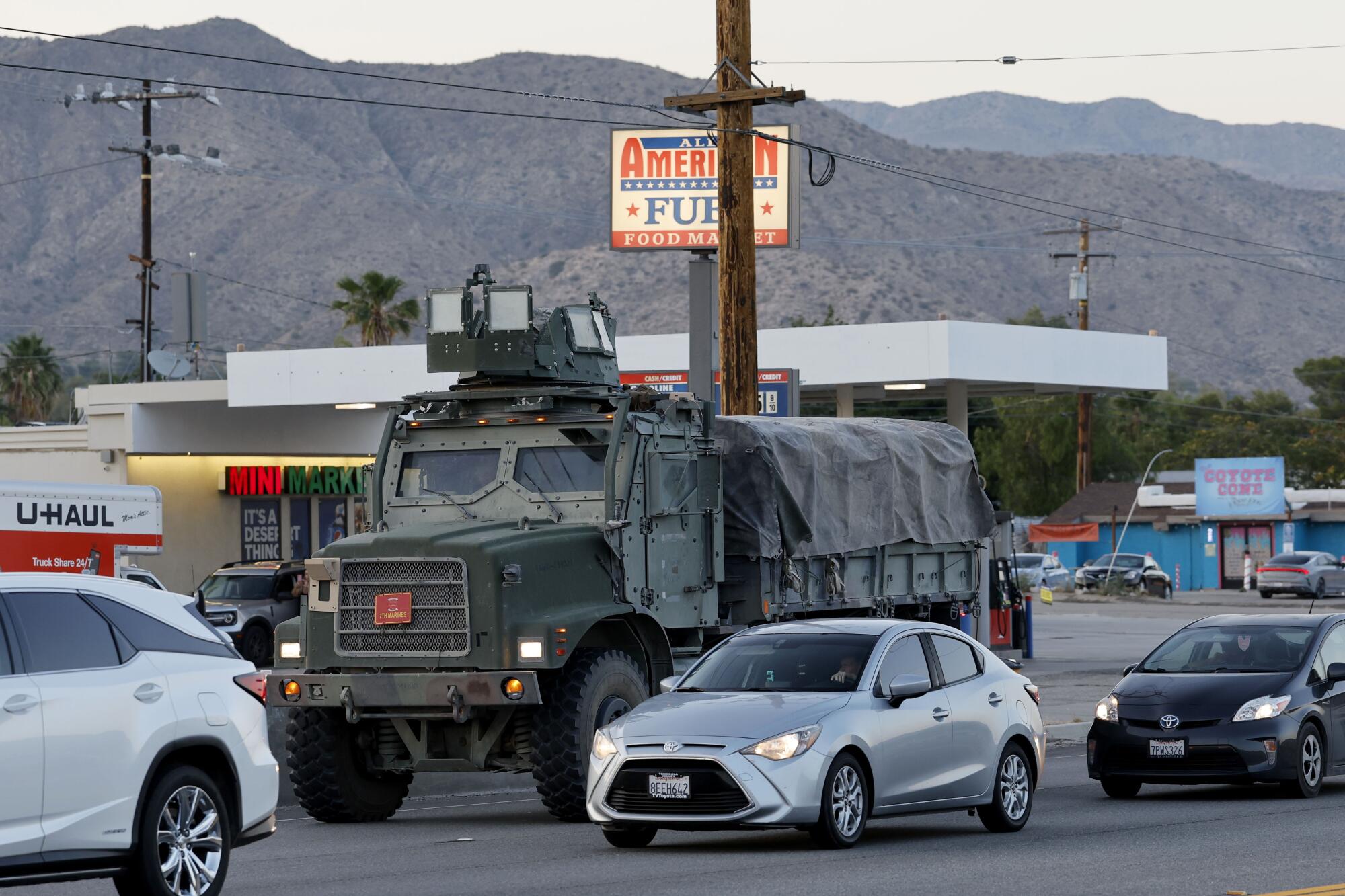 A military truck joins other vehicles driving past a gas station