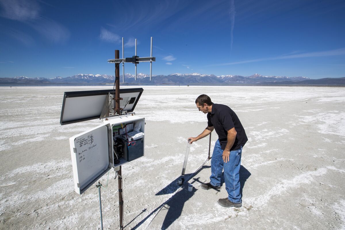 A man uses a tube-like device to measure dust on a salt playa.