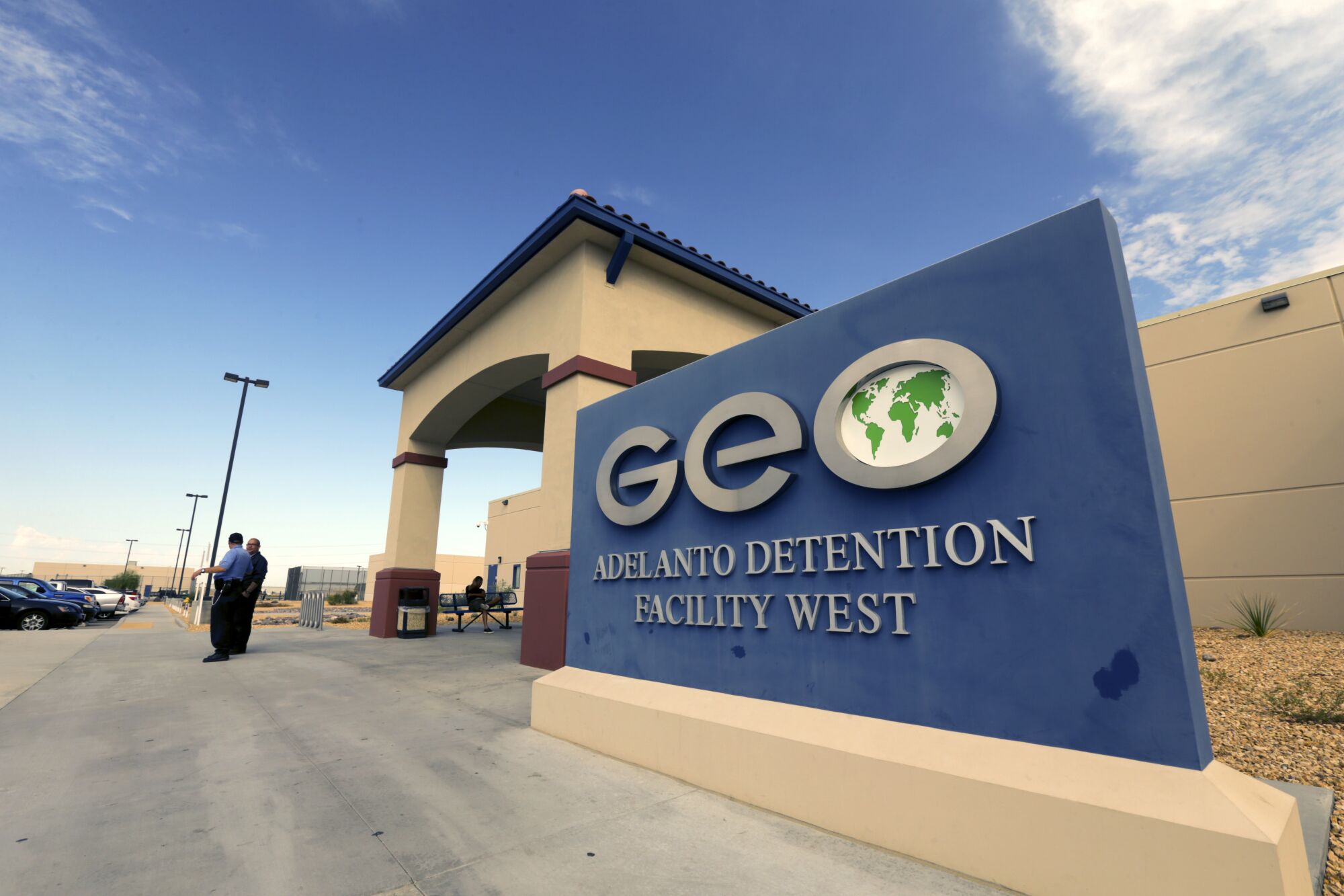 A blue sign that reads GEO Adelanto Detention Facility West outside a building