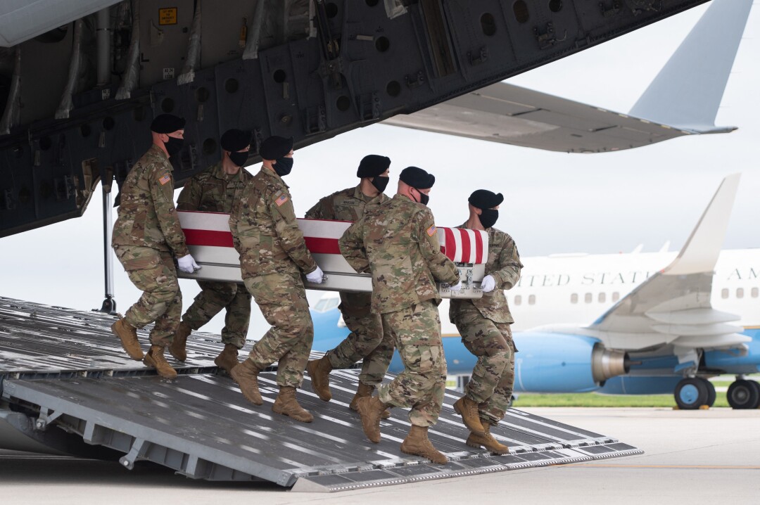 A flag-draped case with the remains of Army Staff Sgt. Ryan C. Knauss are carried off a military aircraft by servicemen.