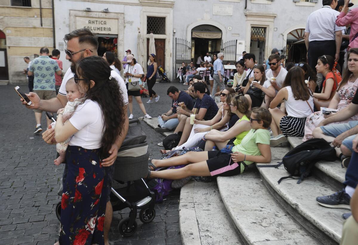 A crowd of tourists sit on steps and take selfies near the Pantheon in Rome.