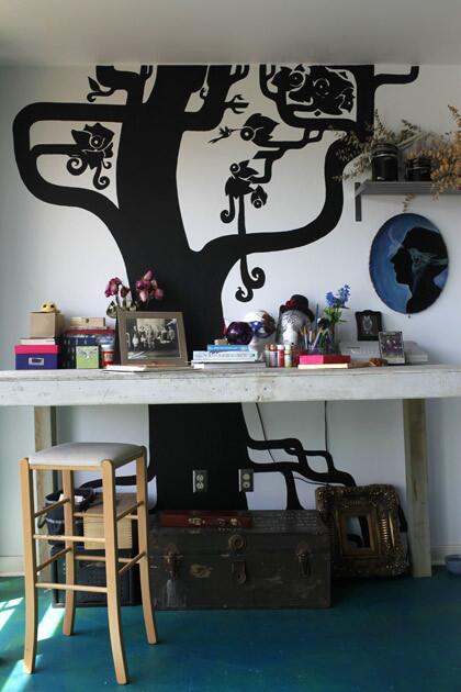 By James Gilden It seems almost inevitable that a theater set designer would have a home that is theatrical. Such is the case for musician and artist Anna Karakalou and musician husband Panos Skourtis. They saturated their apartment with color and graphic designs, including this tree growing by a work table off the kitchen. Karakalou painted the trunk and branches with chalkboard paint, so the wall could be used for keeping score of games. An old Army trunk underneath is full of pinups from the 1940s and '50s.