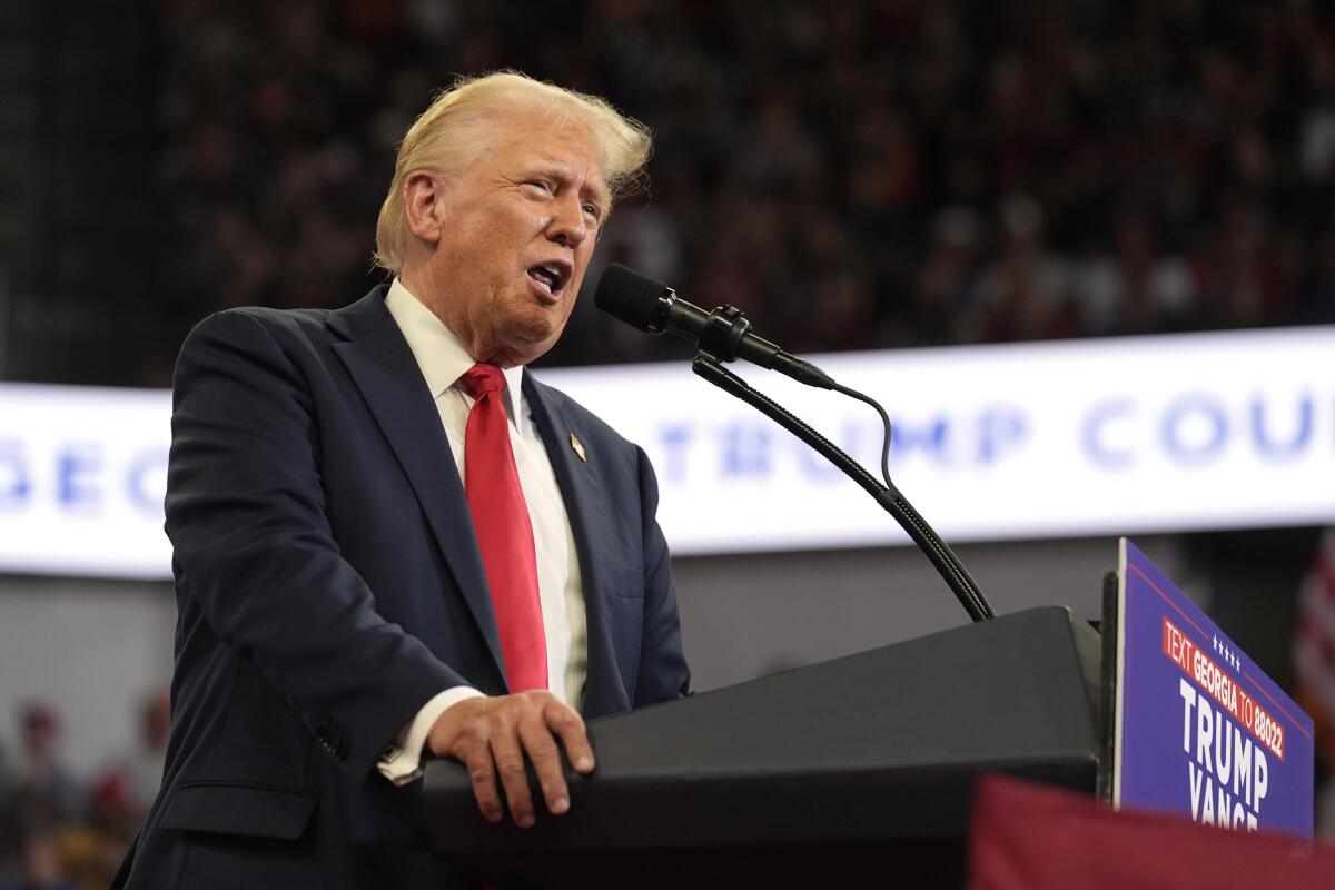 Donald Trump grips the side of a lectern as he speaks in a large venue