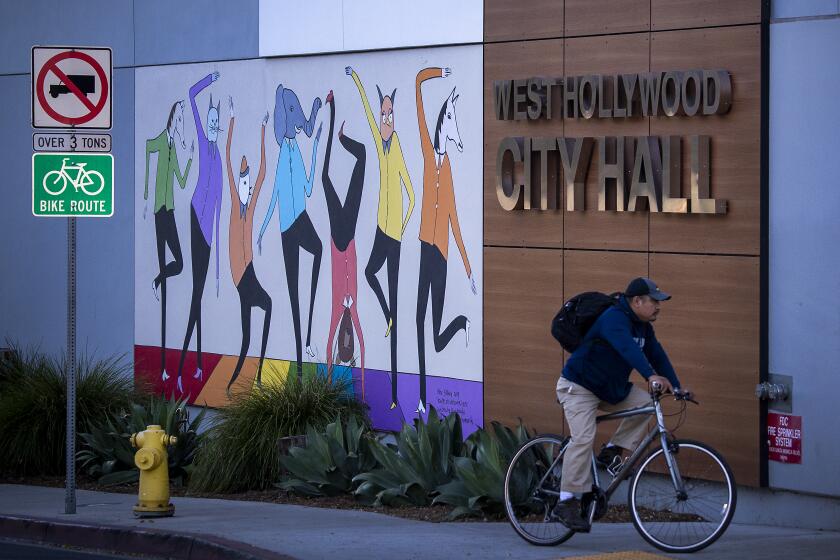 West Hollywood, CA - October 28: A person on a bike rides past the West Hollywood City Hall along Santa Monica Blvd. in West Hollywood at sunset Thursday, Oct. 28, 2021. (Allen J. Schaben / Los Angeles Times)