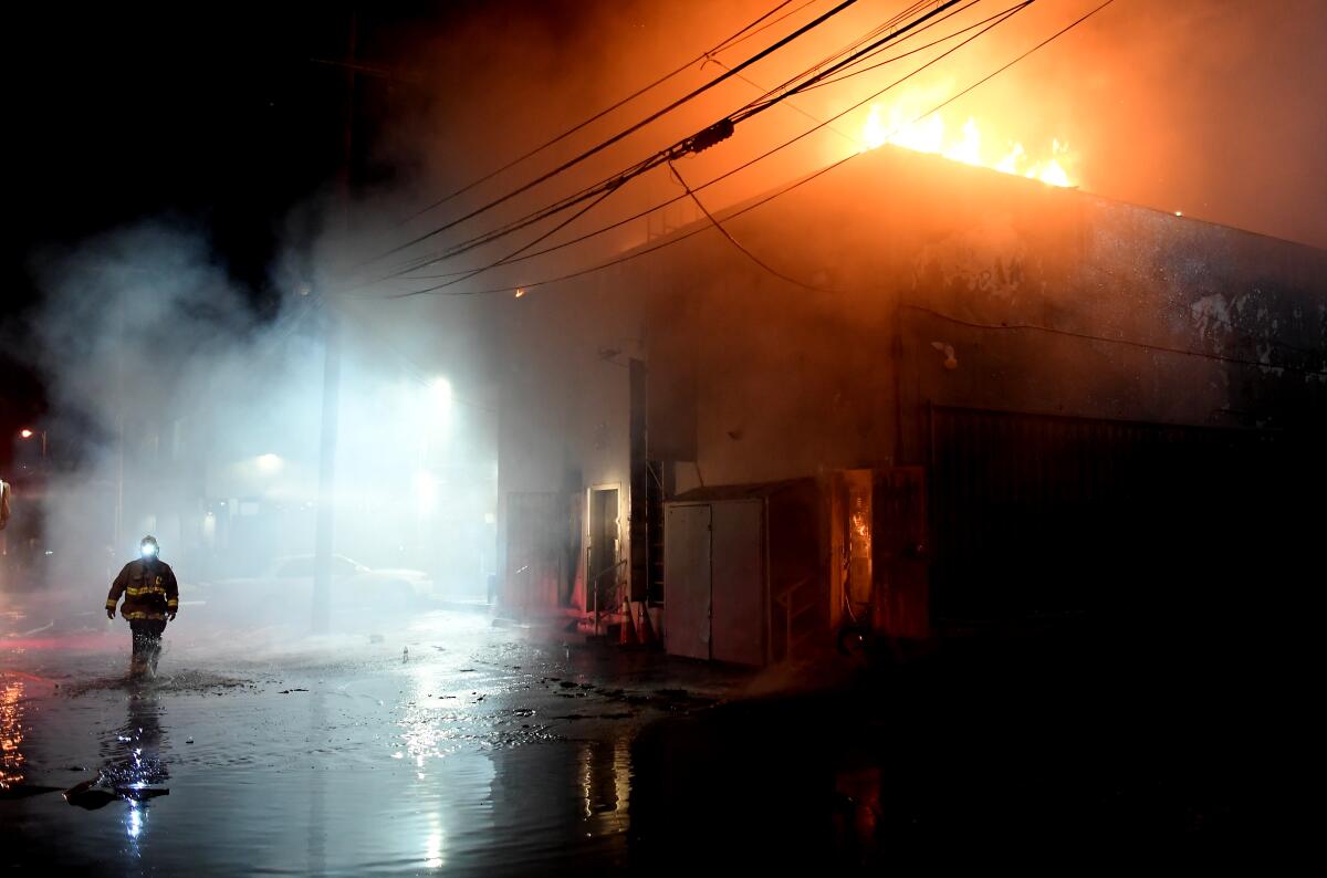 A firefighter walks behind a burning building on Melrose Avenue during civil unrest in Los Angeles on Saturday. 