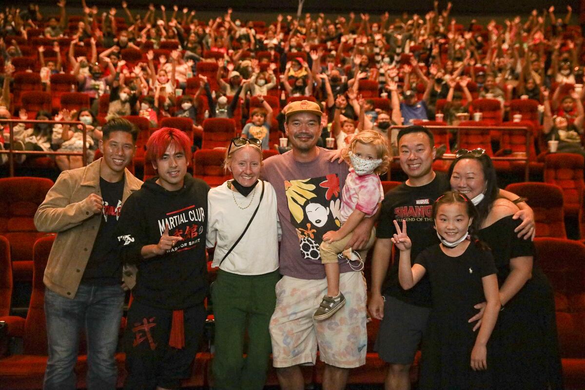 A group of people posing in front of a theater full of people with their arms in the air