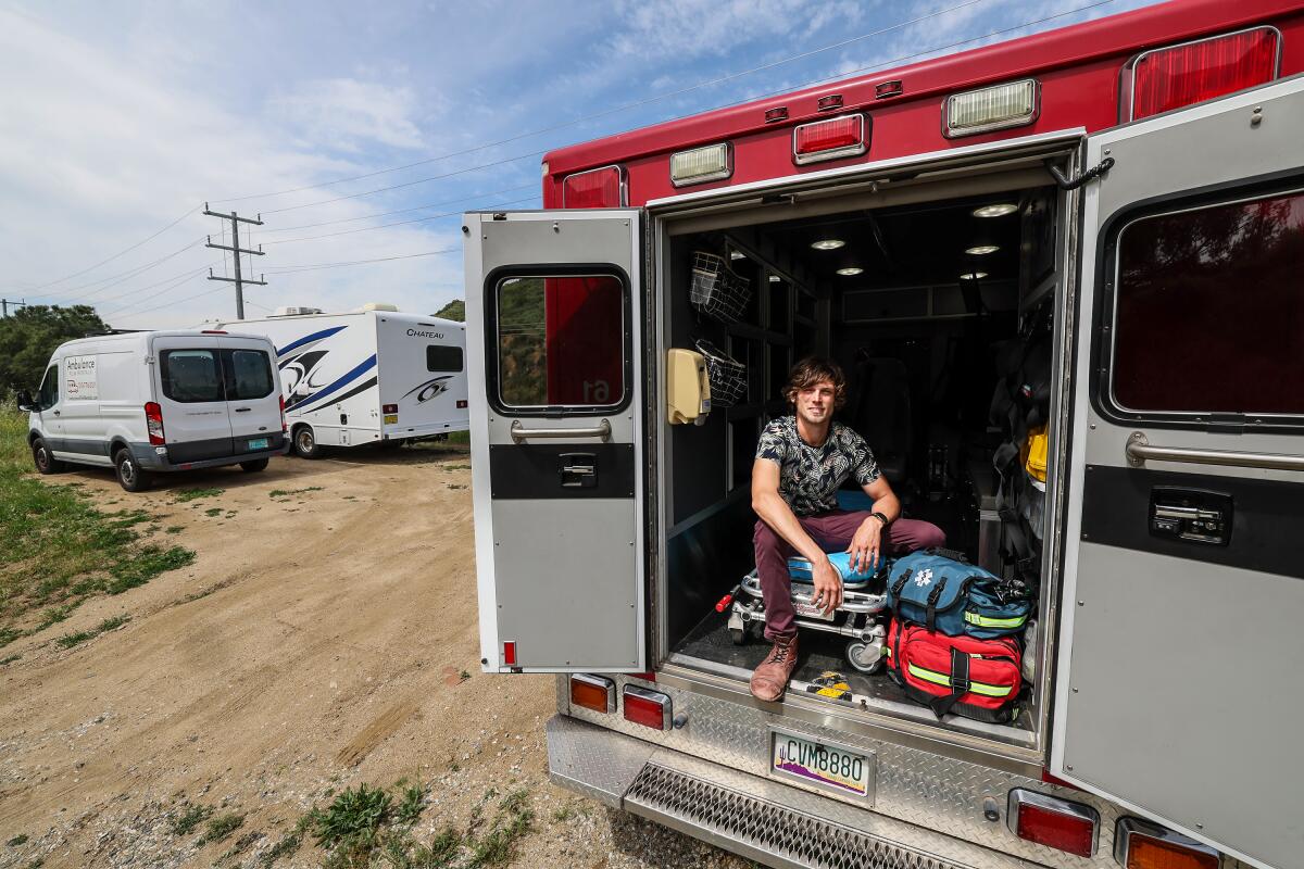 A man sits in the back on an ambulance with its doors open.