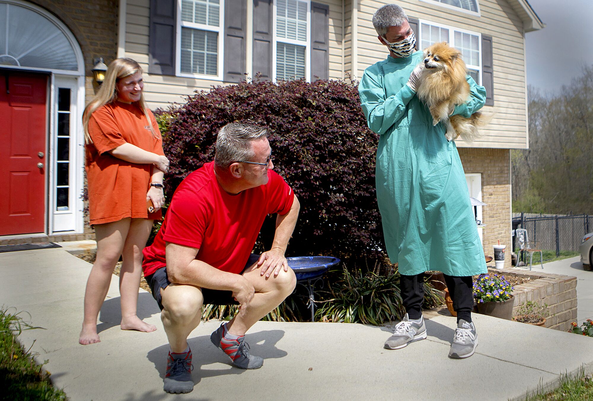 U.S.: Ooltewah Veterinary Hospital Dr. Micah Woods holds Izzy as owners Ken, center, and Zoe Leslie look on at the Leslies' home March 27 in Ooltewah, Tenn. Because of the coronavirus outbreak, Ooltewah Veterinary Hospital began to offer house calls for clients who are unable to leave their homes.