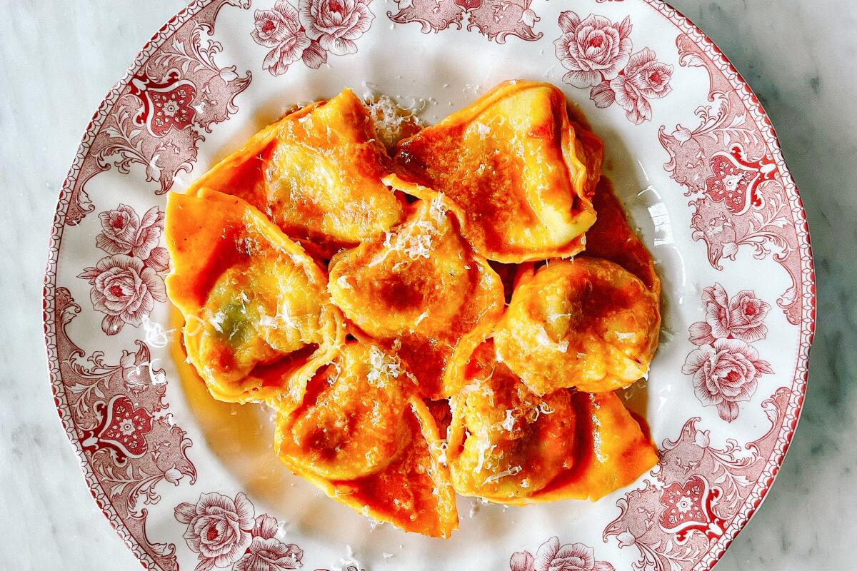 Tortelloni in a tomato and butter sauce served in a red-and-white patterned bowl.