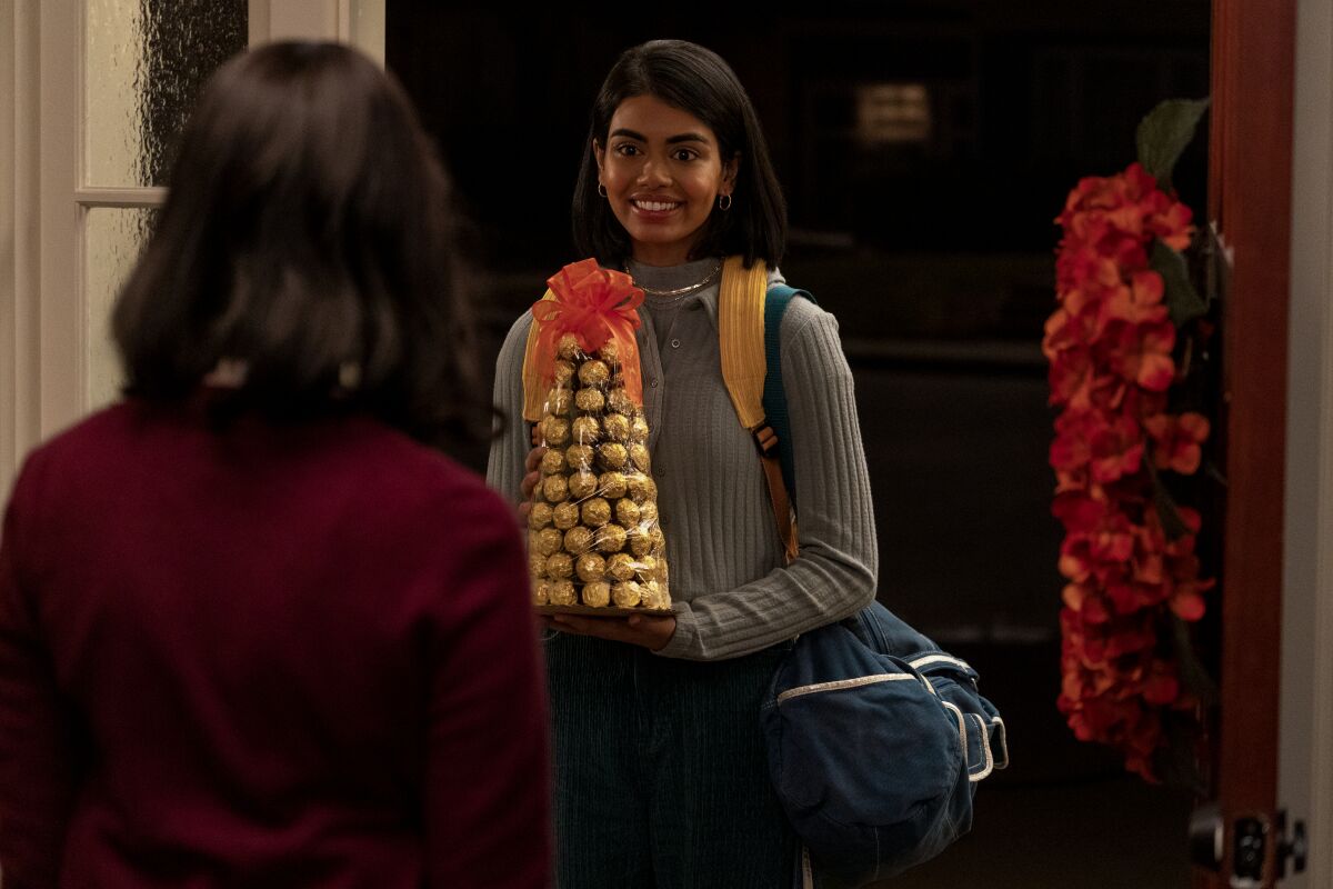 A teen girl stands at a door holding a gift of fancy chocolates